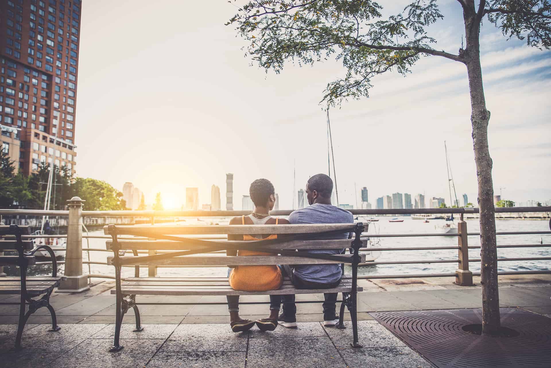 Couple holding hands in a bench while watching the sunset, image of love & relationships category from Harvesting Happiness Talk Radio.