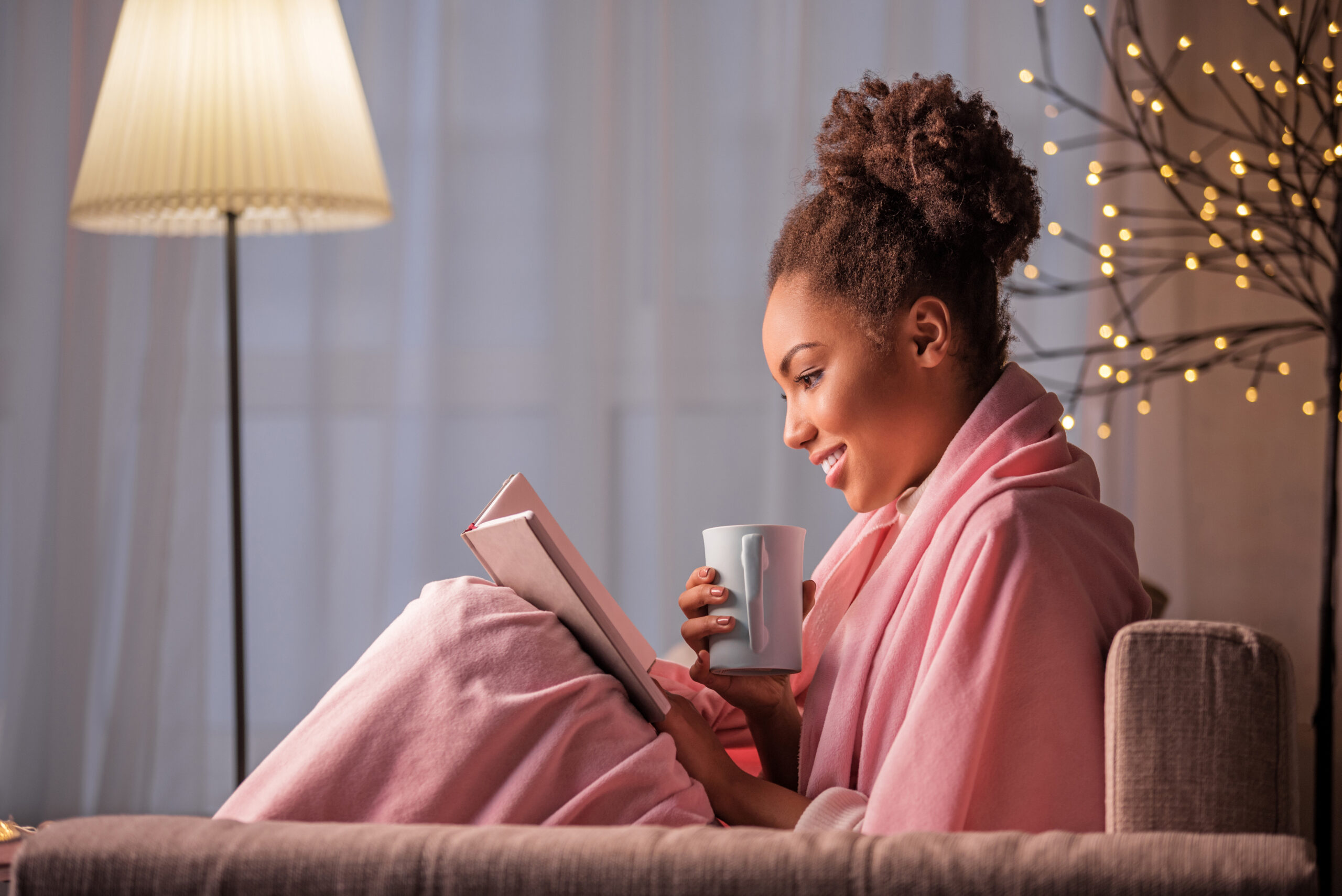 Woman with brown hair and a pink blanket reading on a book image of new podcast episode of Harvesting Happiness Talk Radio about dissonance, fear and peace with Panache Desai & Humble the Poet