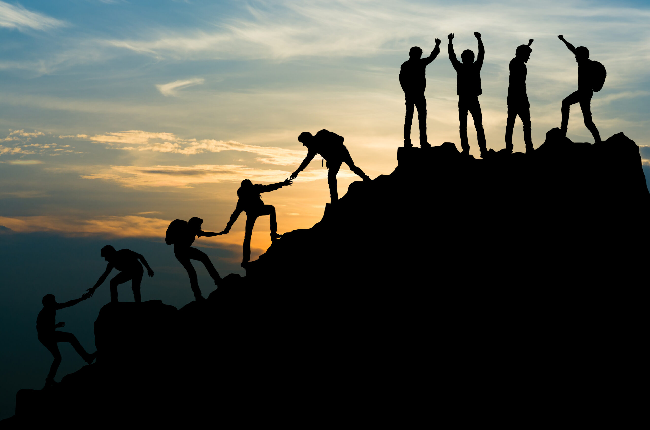 People helping each other climb a mountain with a sunset as background image of new podcast episode of Harvesting Happiness Talk Radio called Lessons in Transformation: Mindful, Positive Leadership with John Perkins & Manny Weintraub