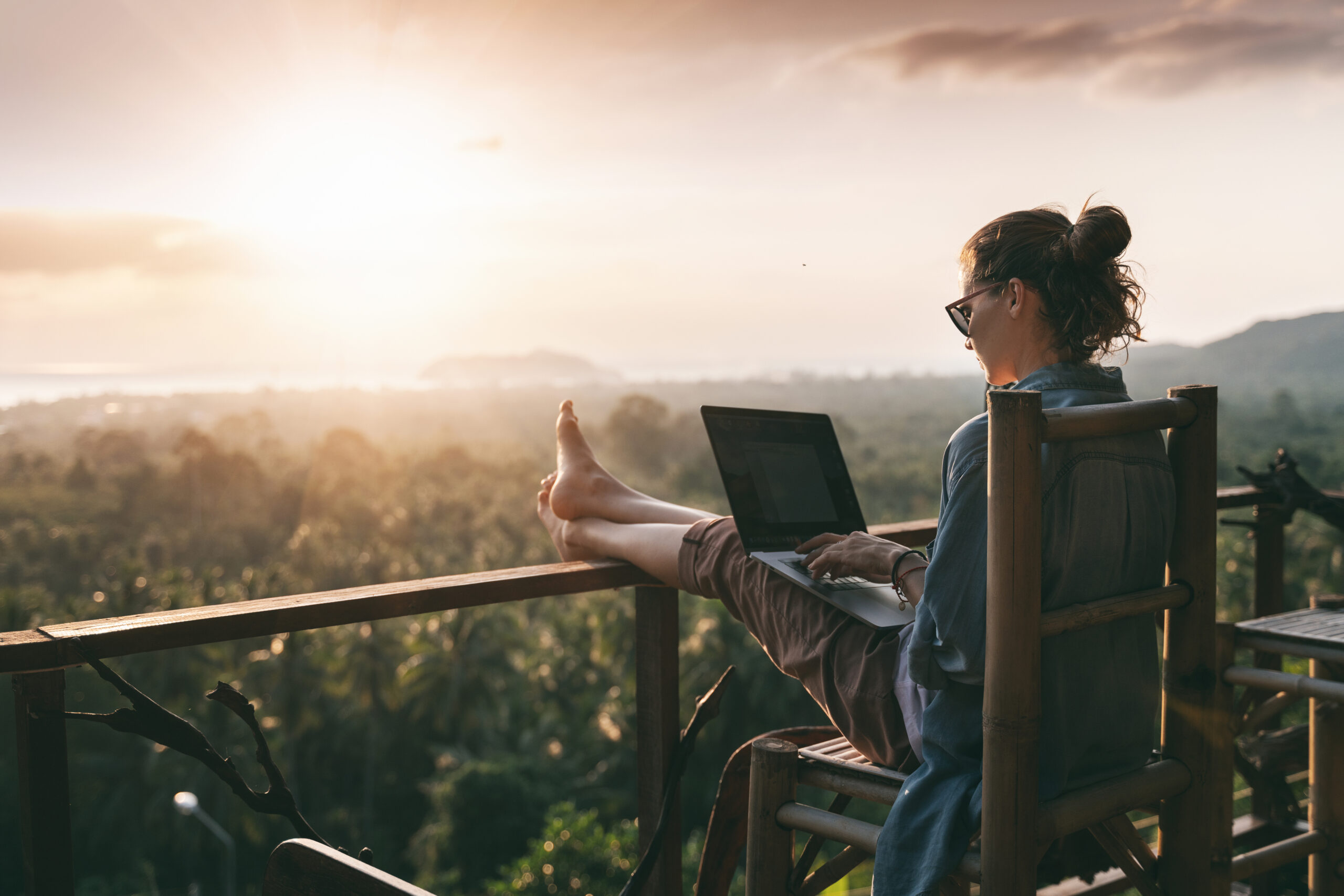 Woman with a blue shirt and sunglasses writing on laptop while watching the sunset, image of new podcast episode of Harvesting Happiness Talk Radio about the reality and bs with Dr. Jodie Eckleberry Hunt & Gary John Bishop