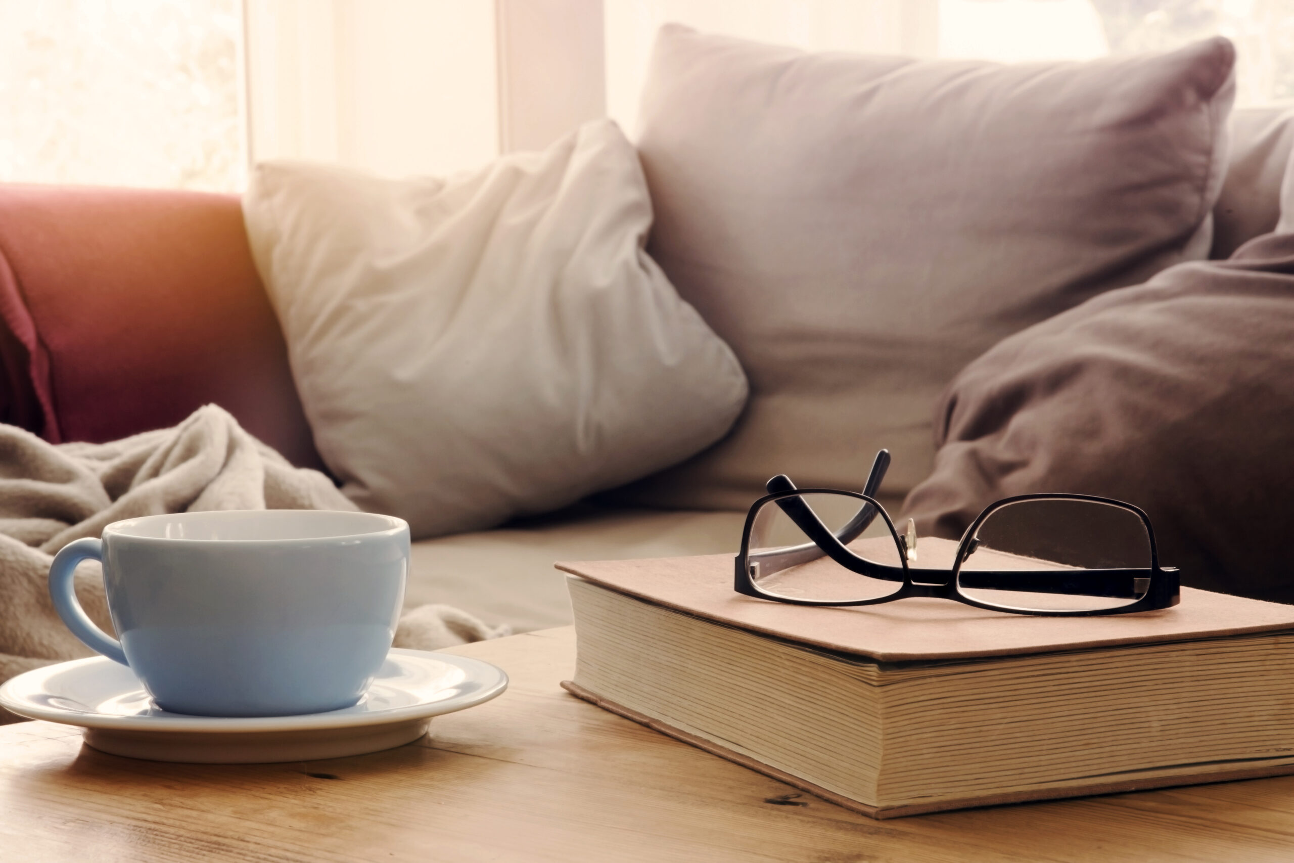 Book with coffee and black glasses on a warm living room with white pillows, featured image of episode about inner work and aging and adulting with Dr. Connie Zweig & Ira Israel